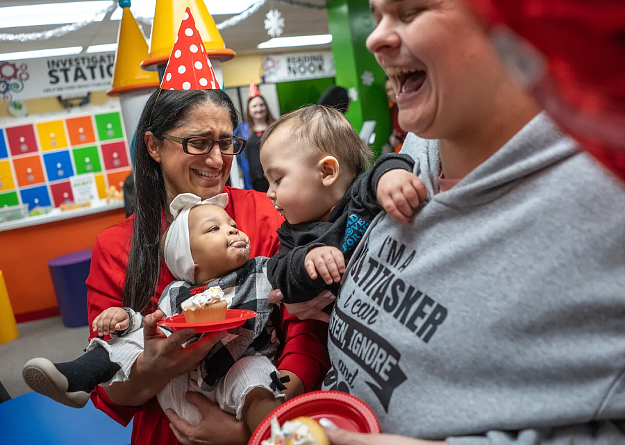 A birthday party with two people each holding an infant who are looking at each other, and the people are holding cupcakes in their hand