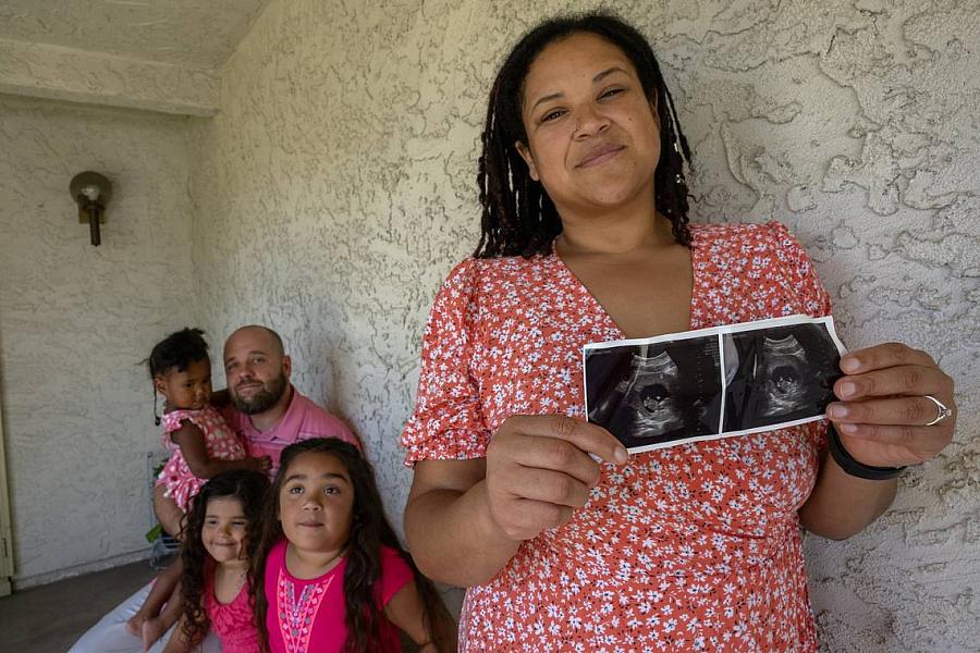 A mom holds a sonogram of her baby while standing with her family 