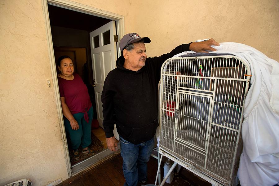 A man adjusts the cover on his parakeet cage as he and wife stand near the front of their home