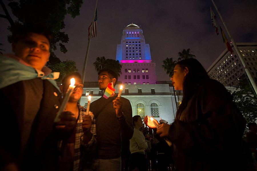 People holding lit candles in evening with LGBTQ+ flag