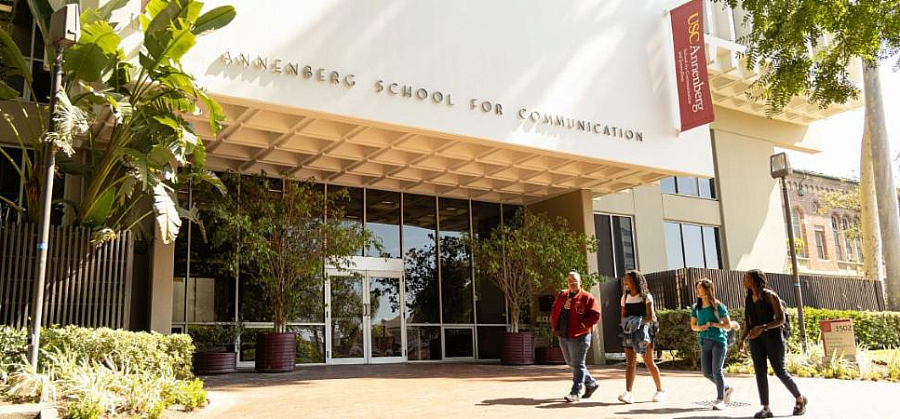 Exterior of the USC Annenberg School for Communication as four students walk past the entrance.