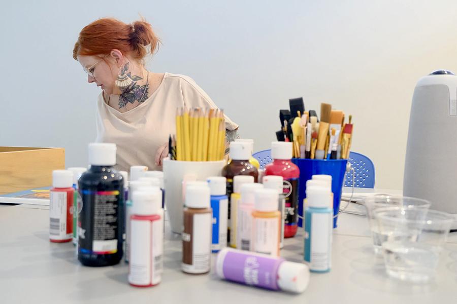 A lady seating beside a table with Paint and brushes on it