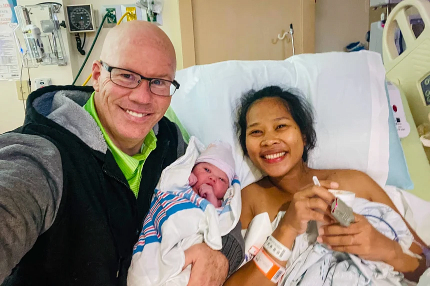 2 people smiling, one holding a newborn