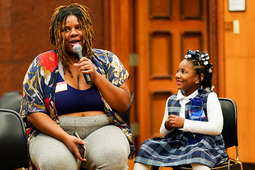 Person speaking into a mic while a child watches