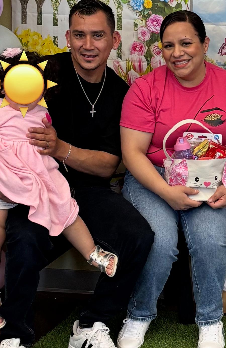 A couple sits smiling with their daughter on their lap