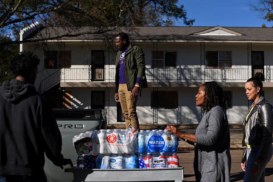 Residents place cases of water on a vehicle.