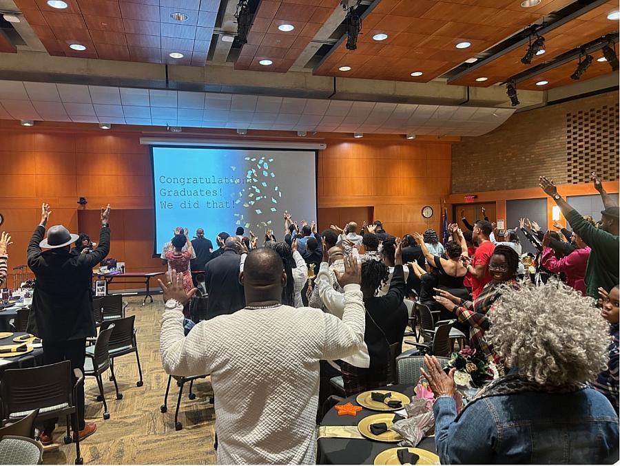 People raising their both hands looking at the screen that says "Congratulations graduates! We did that!"