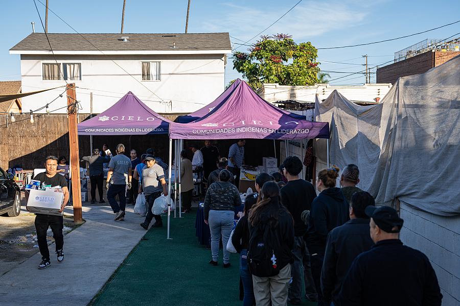 Folks wait in line outside of a purple tent waiting for distributions from CIELO
