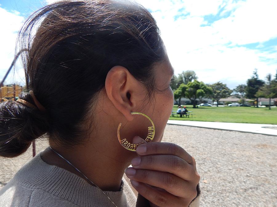 A woman with dark hair shows off her earrings that say Powerful Women in Spanish