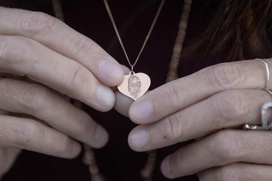 Hands holding a necklace with a thumbprint