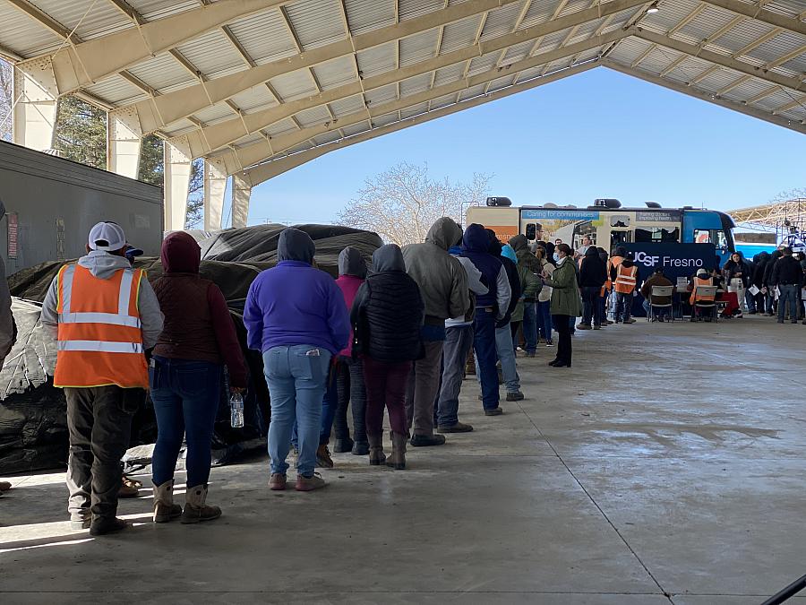 Farmworkers line up for medical care at UCSF Fresno's mobile clinic under a large outdoor wooden structure