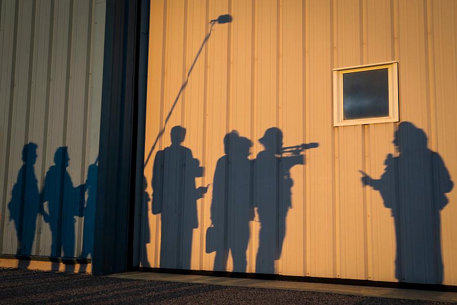 Silhouette of reporters shown against the wall of a hangar. 