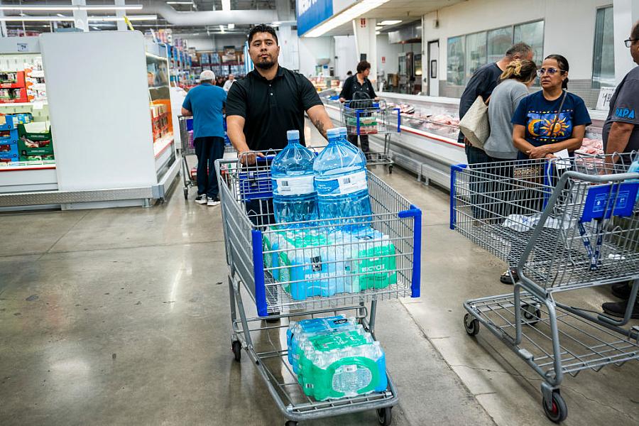 A man pushes a shopping cart filled with bottled water.