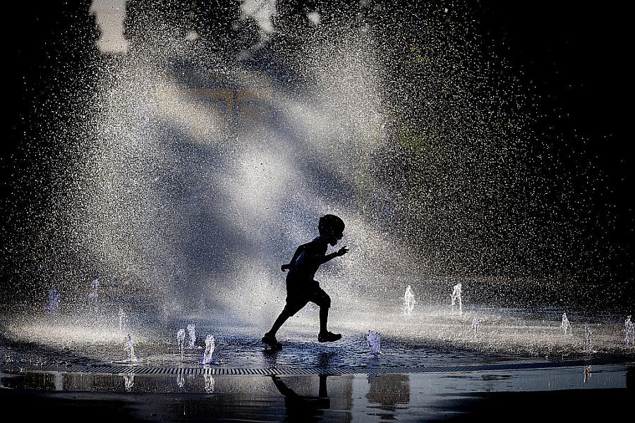 A young boy runs through a fountain.
