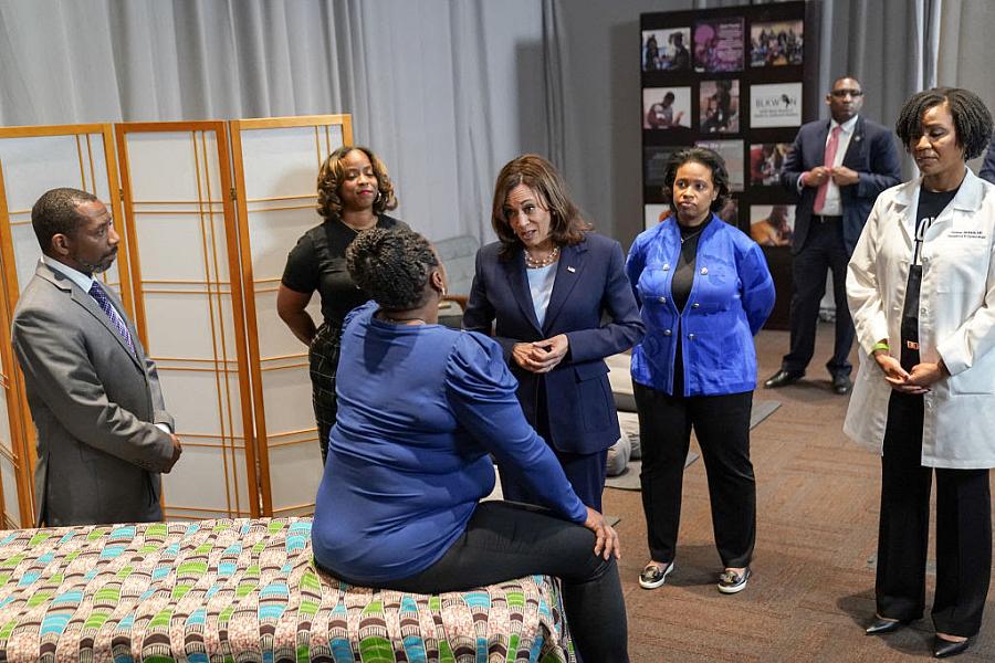 Person seated on a bed talking someone surrounded by people