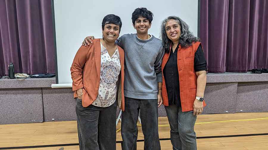 Shreyas Jay with Rcoz Executive Director Sruti Ramnath and Roopali Rajvanshy, founder and CEO stand together in front of a stage with purple curtains at a community event 