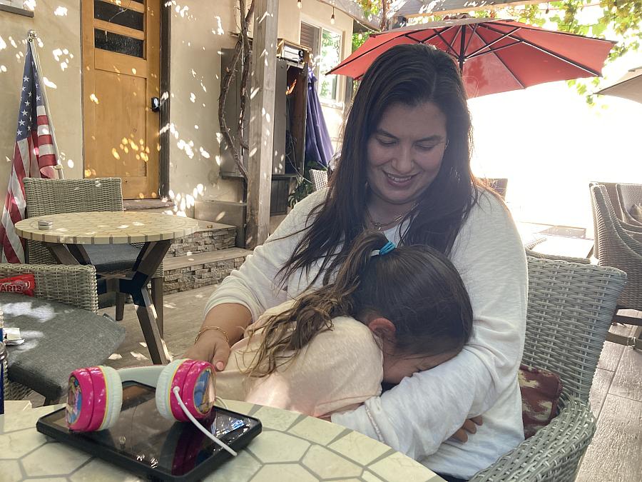 A mother sits on a chair, holding her 6-year-old daughter.