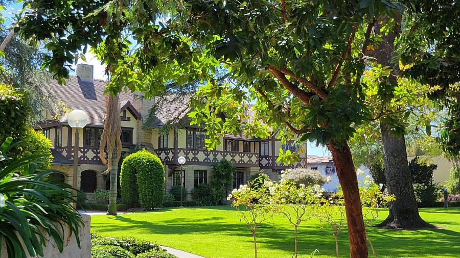Kerckhoff Hall surrounded by lush trees, landscaped gardens, and a sunlit green lawn.