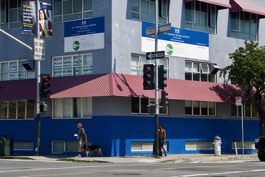 A man and his dog walk past a blue building with a red awning and a sign that says, “St. Vincent De Paul Society Multi Service Center.” 