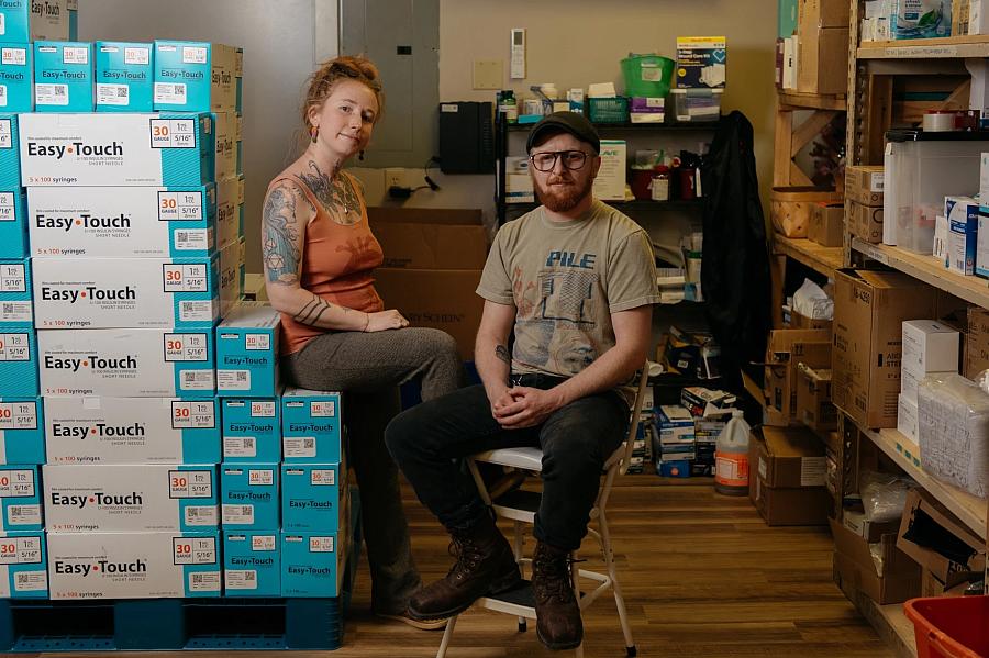 Two people sitting with a stack of needle boxes 