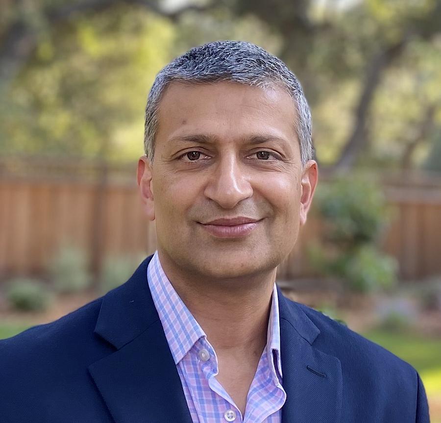 A grey haired Indian man smiles at the camera