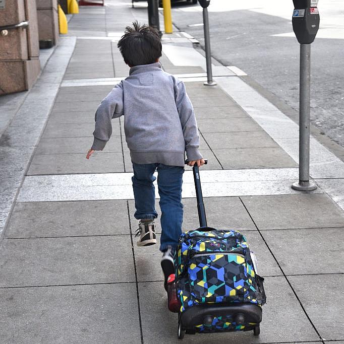 Young person running on a pavement dragging a bag with wheels