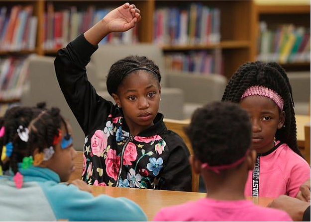 A child, sitting with other children, raising hand