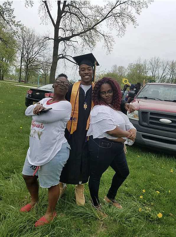 3 people standing together, one in a cap and gown