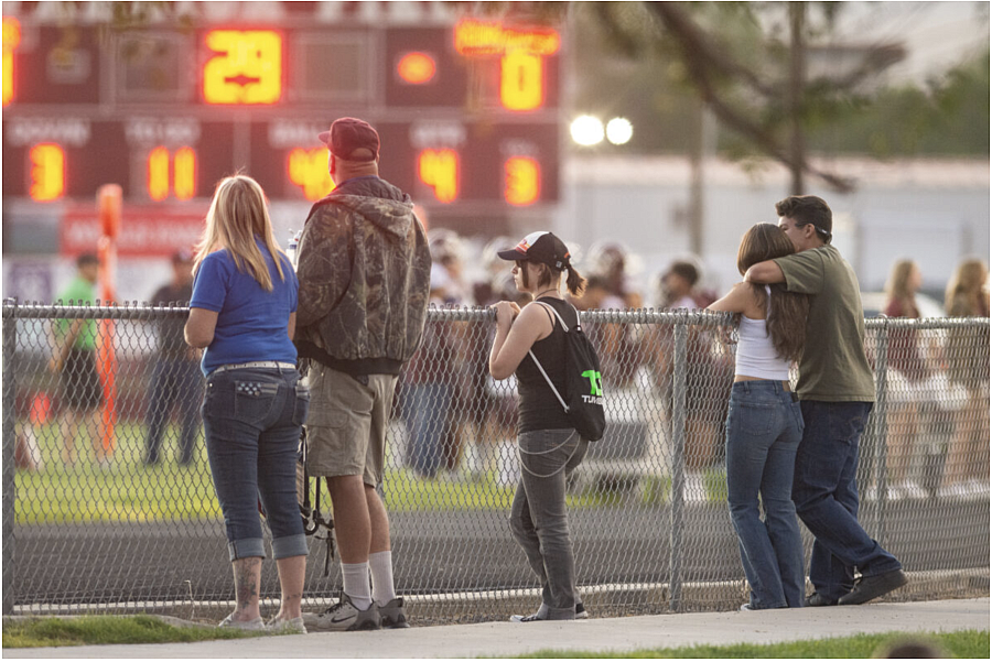 People behind a metal fence, a score board in front of them