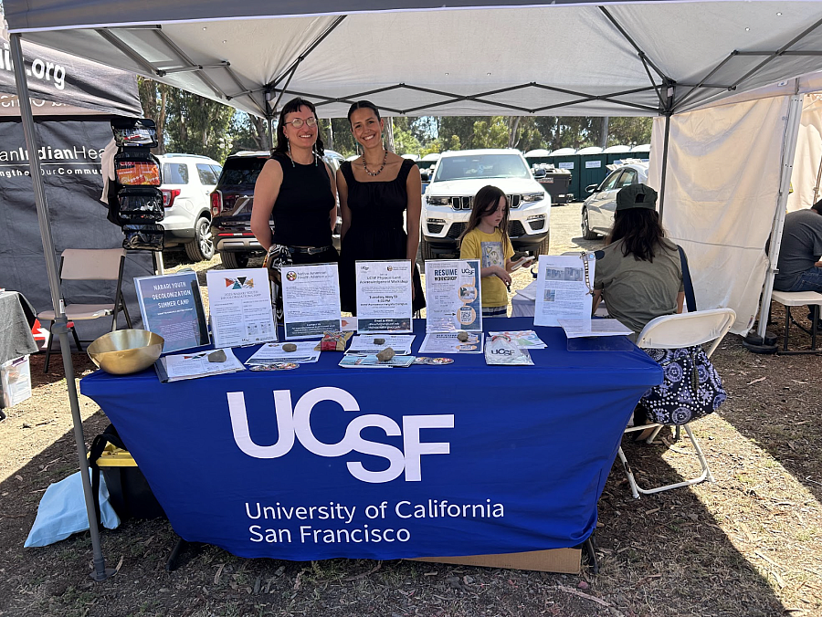 Two women stand at a booth for the Native American Health Alliance for UCSF