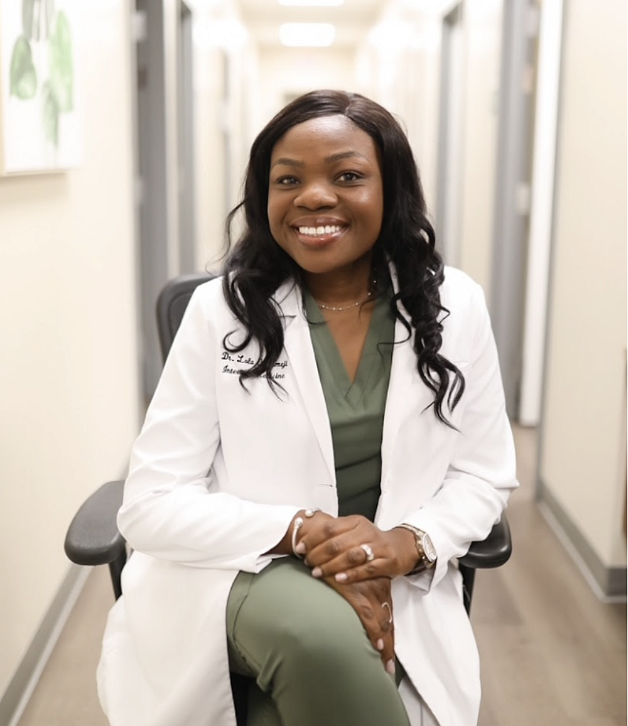 Dr. Ololade Oladimeji, a Black physician, smiles and sits in her white coat