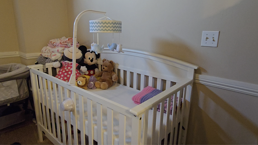 A white crib with plush toys sits empty in a nursery.