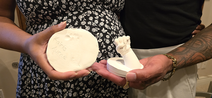 A Black couple's hands holds plaster molds of their late daughters hand and foot.