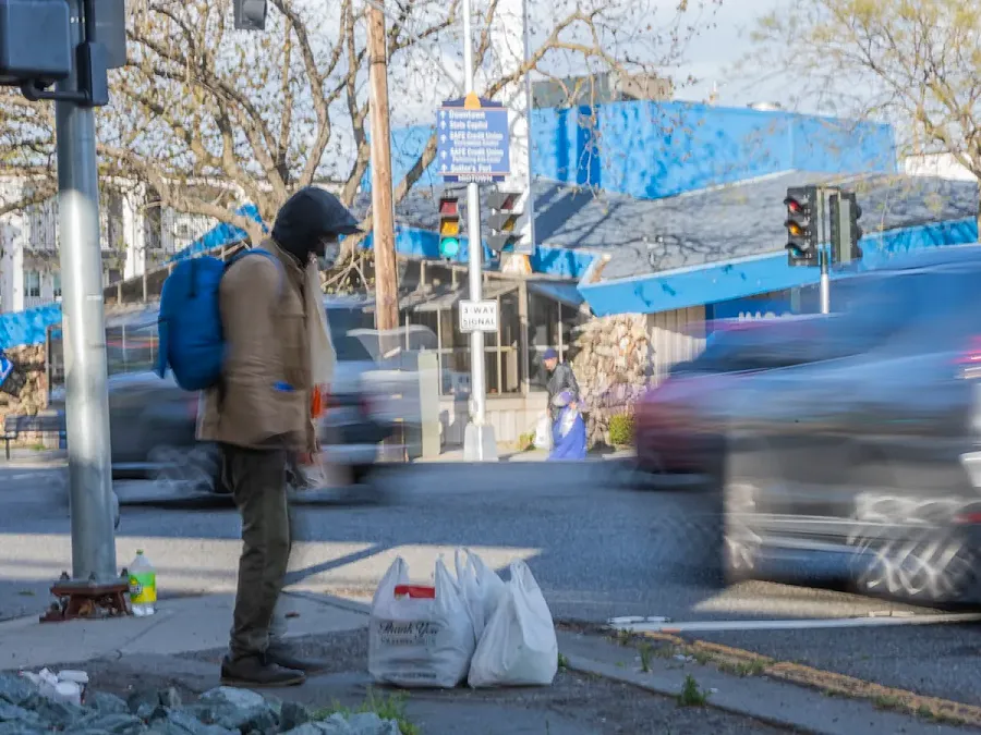 Person standing on a pavement with two plastic bags besides them