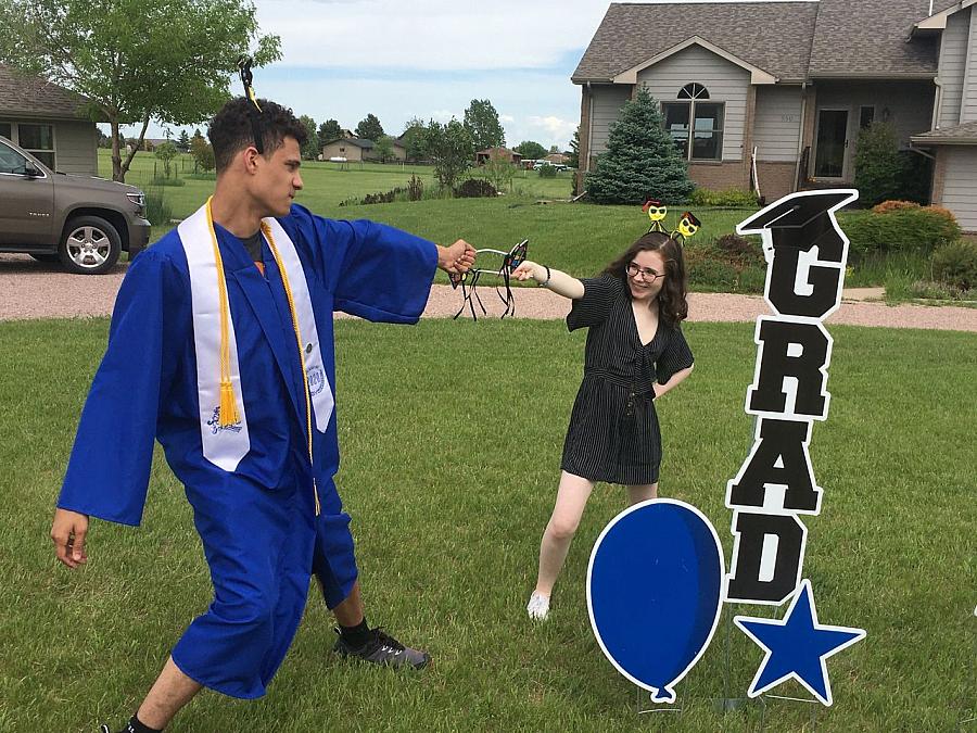 2 people smiling, one in a cap and gown. A 'grad' sign beside them