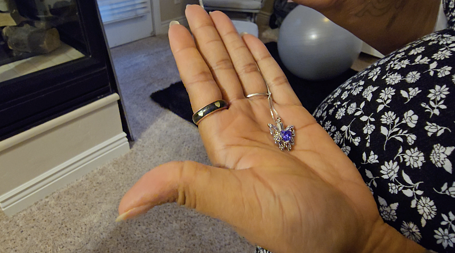 A Black woman's palm holds a silver and purple butterfly necklace that will carry the remains of her daughter.