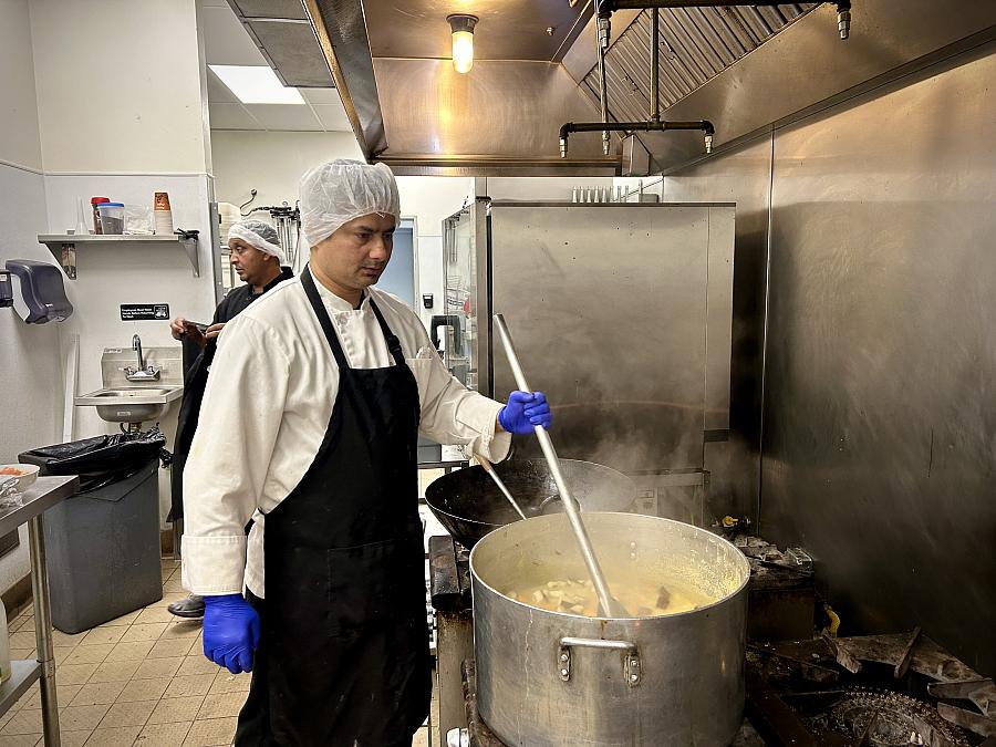 Person wearing an apron and hair net, stirring food in a pot