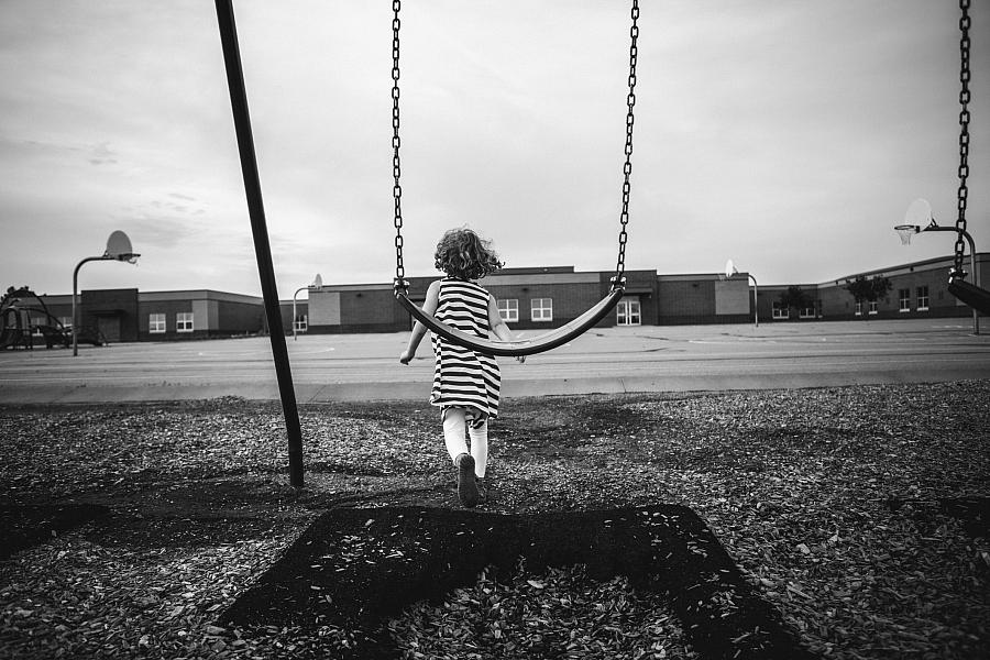 Black and white picture of a child walking away from a swing