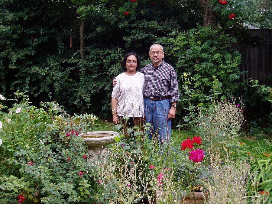 An older Indian couple stand in a garden full of flowers in London.