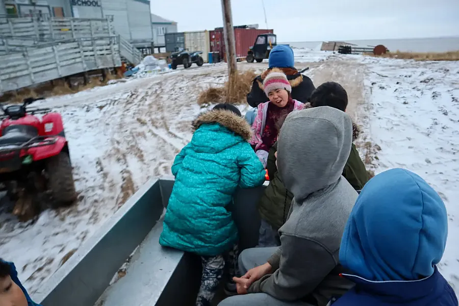 Children bundled in winter clothes ride in a trailer, known as the “bathroom bus,” through a snowy rural village.