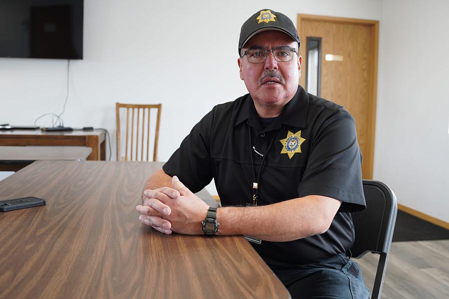 A man in a black sheriff uniform sitting at a table, possibly a law enforcement officer being interviewed or giving a statement.