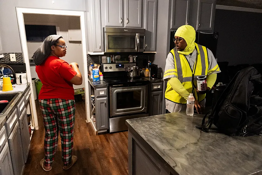 Two people standing in kitchen, one wearing a red top and other in yellow reflective suit