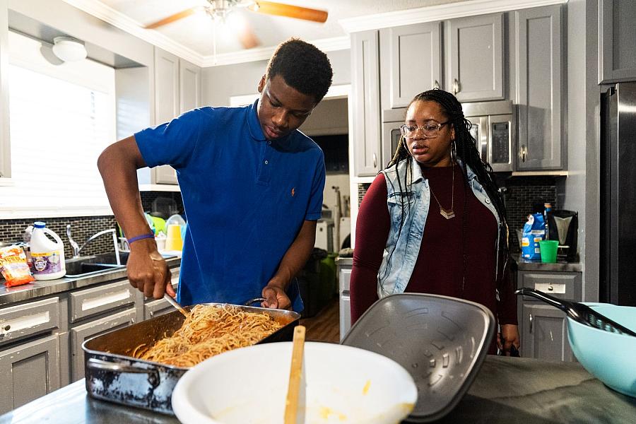 Person making spaghetti with another person overlooking them