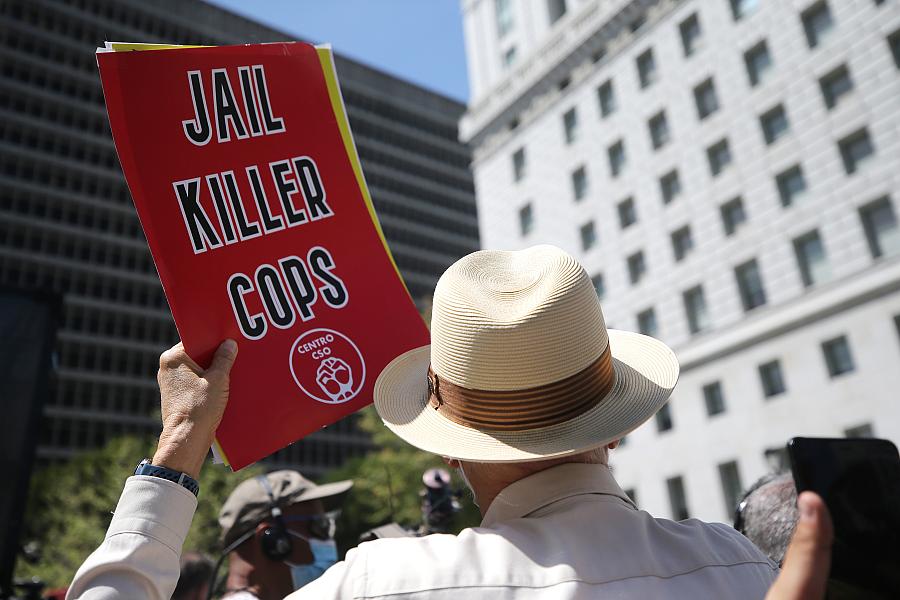 A person in hat holding banner saying "Jail Killer Cops"