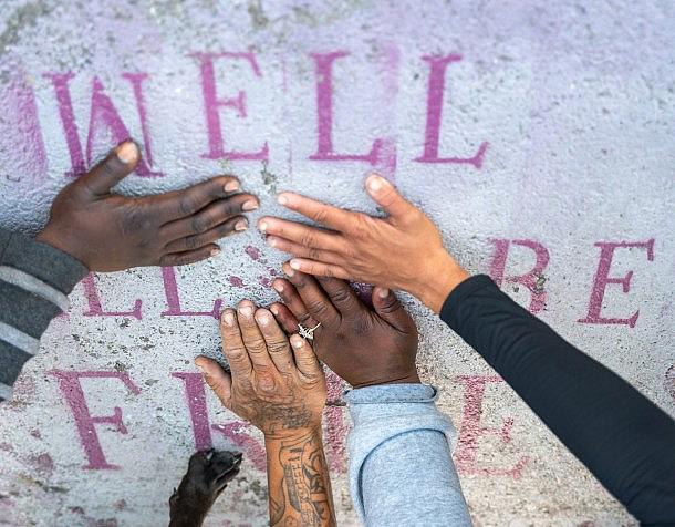 People placing their hands on a saying painted on a wall