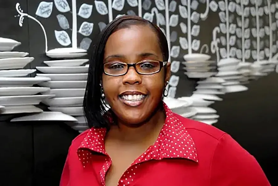 Person with red top and specs standing against a decorative wall