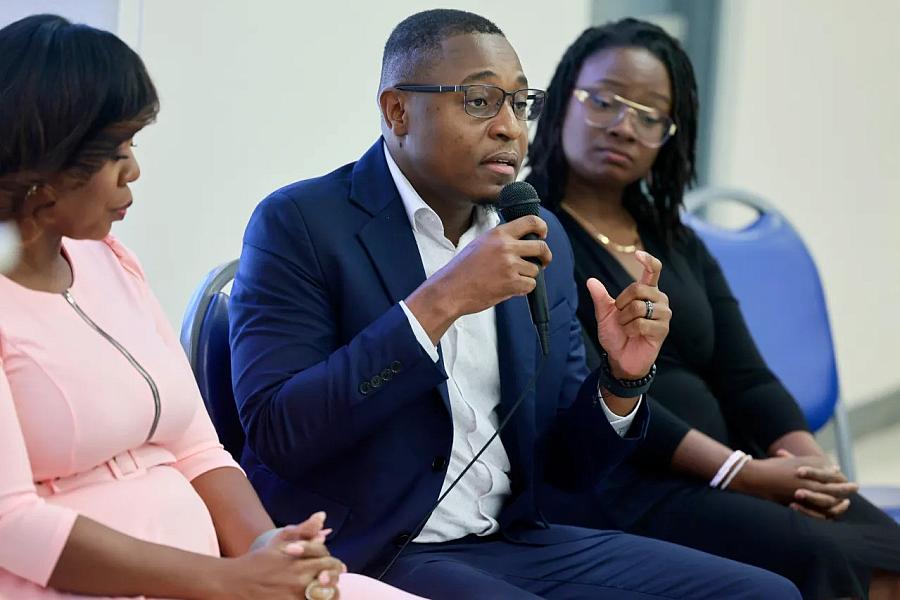 3 People sitting on chairs, one speaking into a microphone