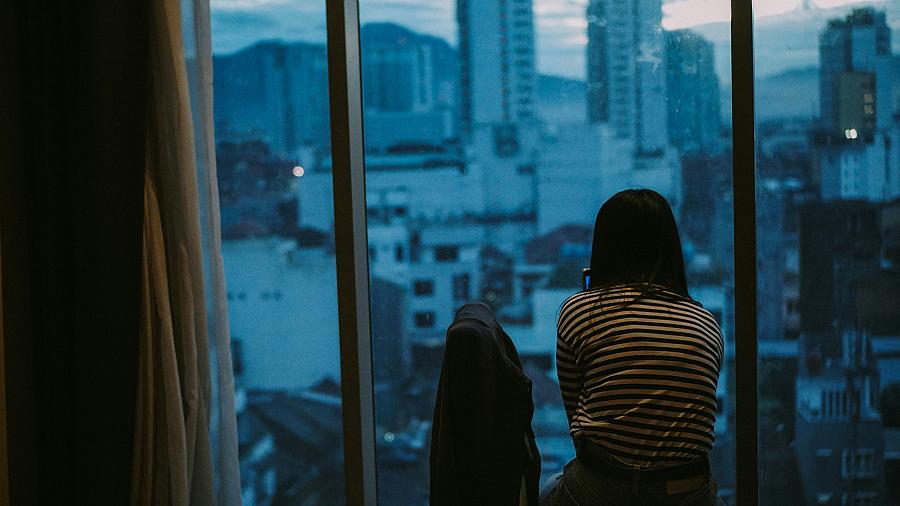 A woman stares out an apartment window.