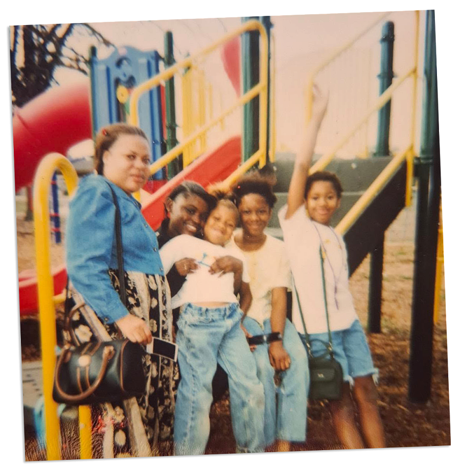Woman and five kids at a playground, one child raising their arm.