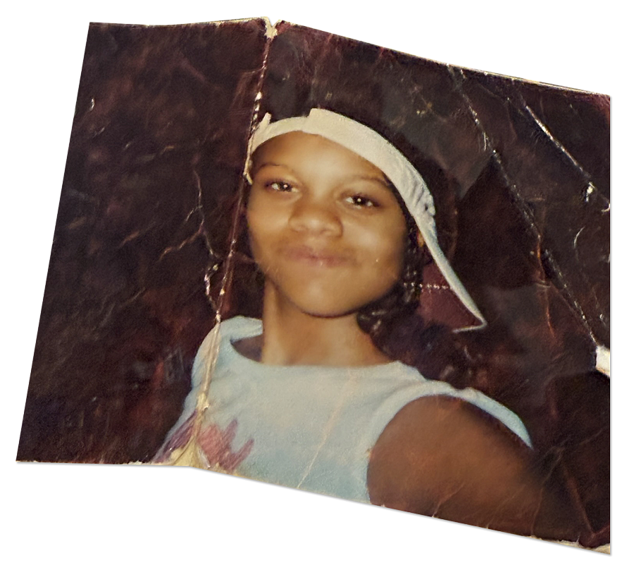 Young girl in cap smiles faintly in a worn, creased photo.